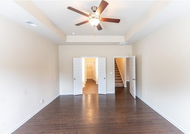 unfurnished bedroom with baseboards, visible vents, a tray ceiling, and wood finished floors