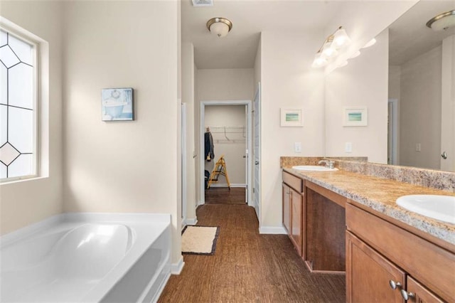 bathroom with a walk in closet, double vanity, a sink, and a bath