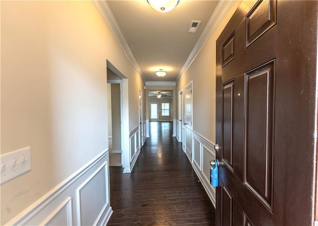 corridor featuring visible vents, wainscoting, dark wood-style flooring, crown molding, and a decorative wall