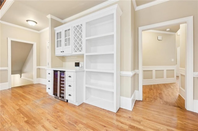 bar with white cabinetry, light wood-type flooring, ornamental molding, and beverage cooler