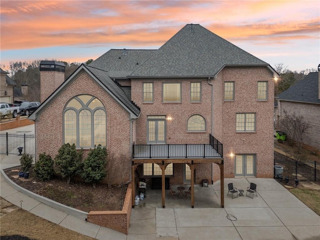 back house at dusk featuring a patio area, a wooden deck, and french doors