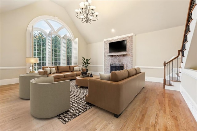 living room with light hardwood / wood-style flooring, a chandelier, lofted ceiling, and a brick fireplace