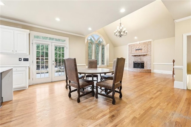 dining room featuring french doors, light hardwood / wood-style flooring, a notable chandelier, a fireplace, and lofted ceiling