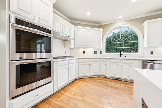 kitchen with decorative backsplash, appliances with stainless steel finishes, sink, white cabinets, and light hardwood / wood-style floors