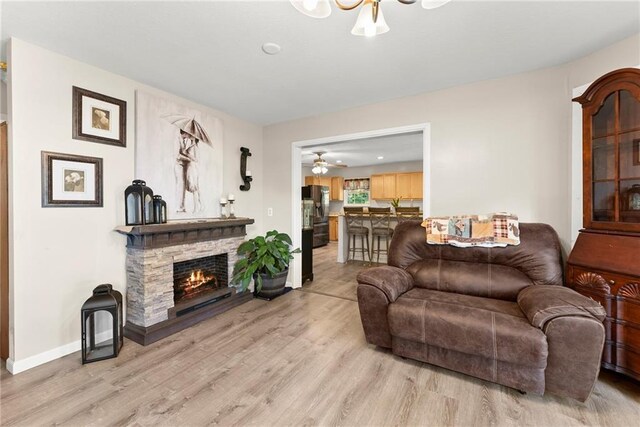 living room featuring ceiling fan, light hardwood / wood-style flooring, and a stone fireplace