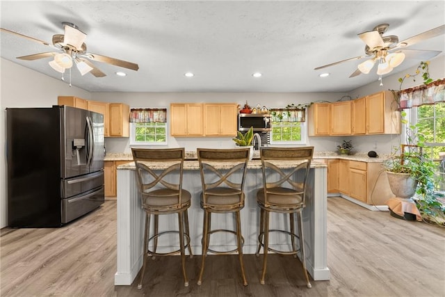 kitchen with a kitchen island with sink, light brown cabinets, stainless steel appliances, and light hardwood / wood-style flooring