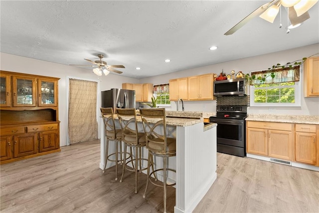 kitchen with light wood-type flooring, appliances with stainless steel finishes, plenty of natural light, and light stone countertops