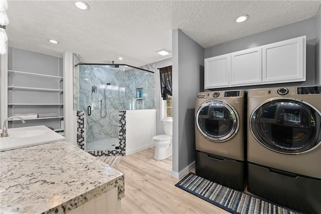 laundry area with a textured ceiling, separate washer and dryer, light hardwood / wood-style floors, and sink