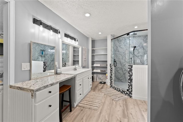 bathroom with wood-type flooring, a textured ceiling, walk in shower, and vanity