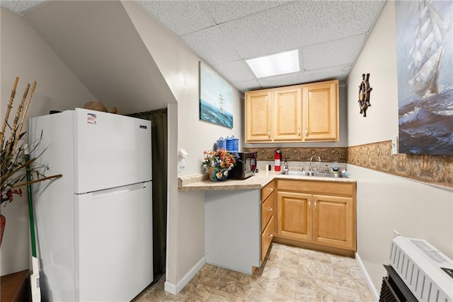 kitchen with a paneled ceiling, radiator, white fridge, light brown cabinetry, and sink