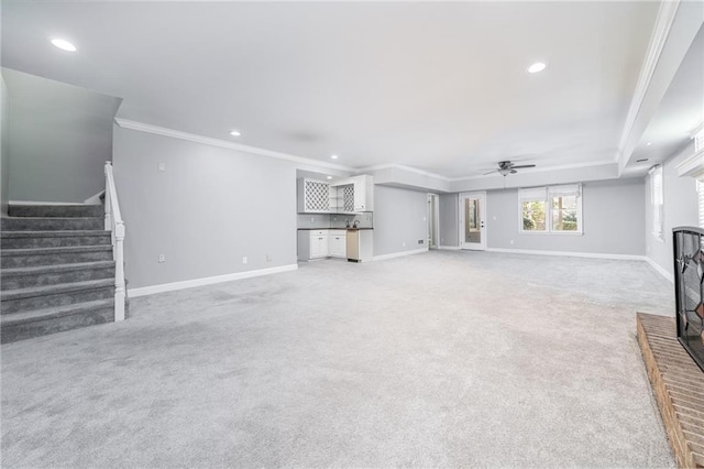 unfurnished living room with ceiling fan, ornamental molding, a brick fireplace, and light colored carpet