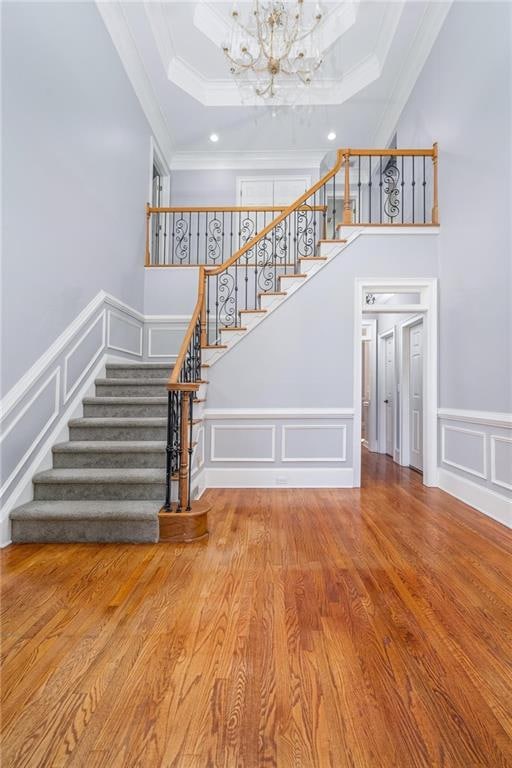 staircase featuring crown molding, hardwood / wood-style flooring, a tray ceiling, and a chandelier