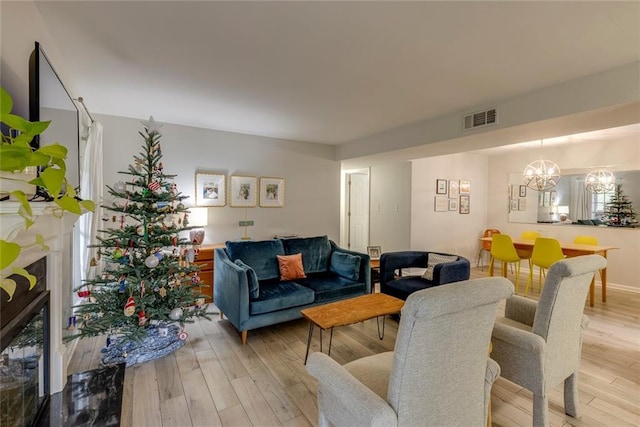 living room with light hardwood / wood-style floors, a premium fireplace, and an inviting chandelier