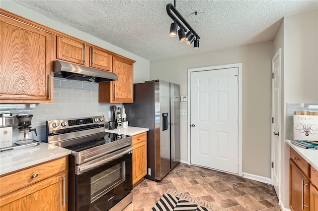 kitchen featuring stainless steel appliances, brown cabinetry, light countertops, and under cabinet range hood