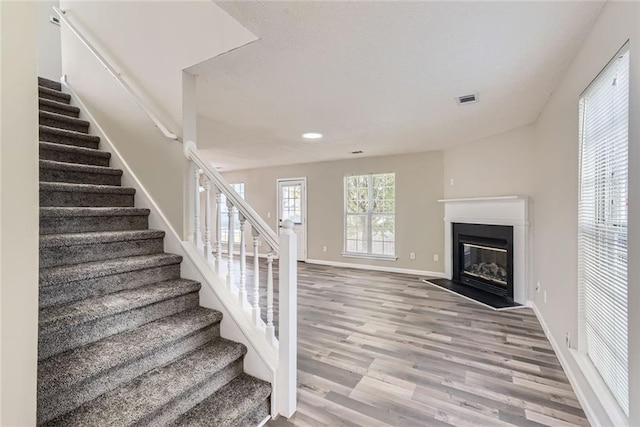 stairs featuring baseboards, a fireplace with flush hearth, visible vents, and wood finished floors