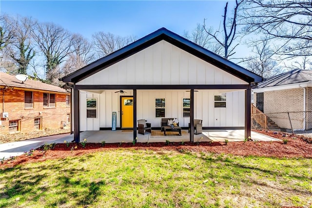 rear view of property with board and batten siding, ceiling fan, fence, a lawn, and a patio area