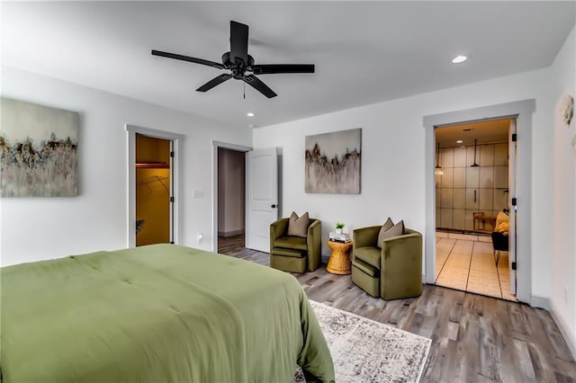 bedroom with recessed lighting, a walk in closet, ensuite bath, and wood finished floors