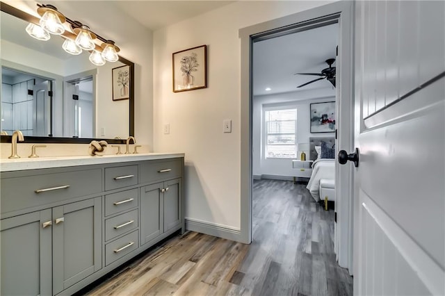 full bathroom featuring ceiling fan, baseboards, double vanity, wood finished floors, and a sink