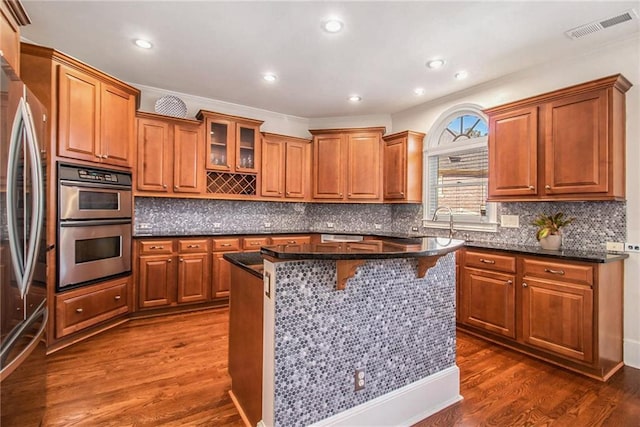 kitchen with dark wood-type flooring, backsplash, stainless steel appliances, a center island, and dark stone counters