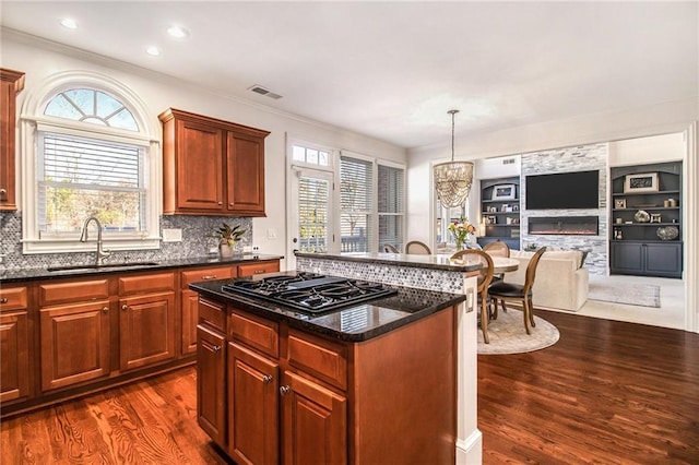 kitchen with a kitchen island, black gas cooktop, sink, dark stone countertops, and hanging light fixtures