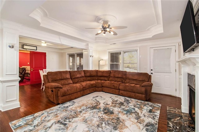 living room with dark wood-type flooring, ornamental molding, a raised ceiling, and ceiling fan