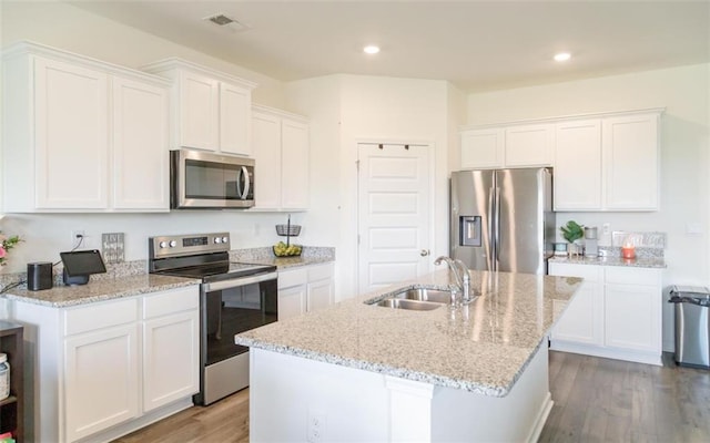 2159 Redfern Rd, Dacula, GA 30019 - kitchen with appliances with stainless steel finishes, wood finished floors, white cabinetry, an island with sink, and light stone counters