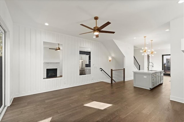 unfurnished living room featuring a fireplace, ceiling fan with notable chandelier, dark wood-type flooring, and sink