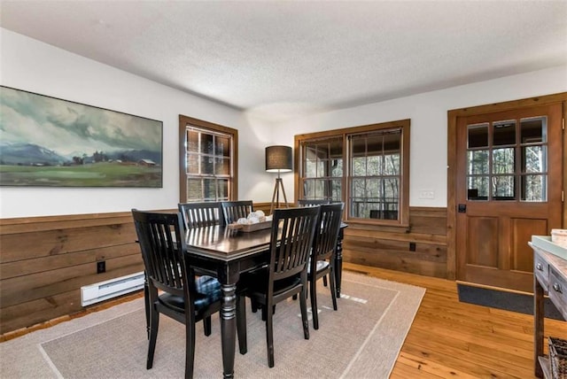 dining area featuring wood walls, light wood-type flooring, a textured ceiling, and a baseboard heating unit