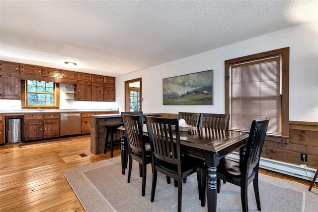 dining room featuring sink, a healthy amount of sunlight, a textured ceiling, and light hardwood / wood-style floors