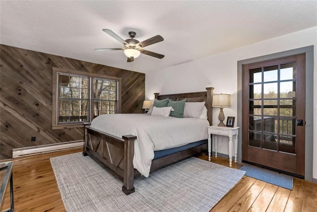 bedroom with wood walls, ceiling fan, a baseboard radiator, and wood-type flooring