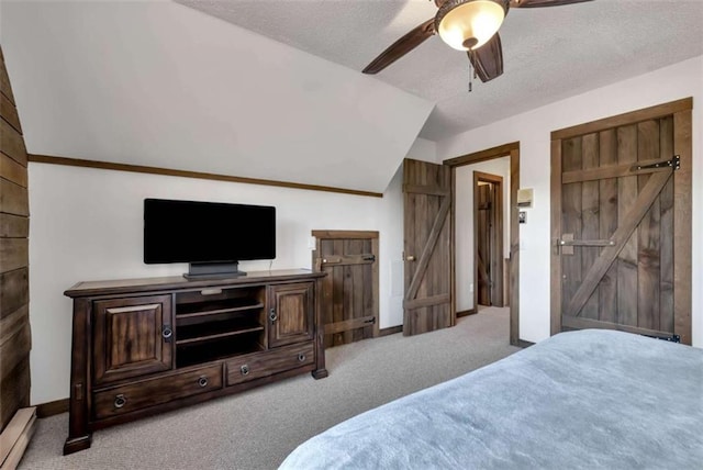 bedroom featuring light carpet, a textured ceiling, vaulted ceiling, ceiling fan, and a barn door