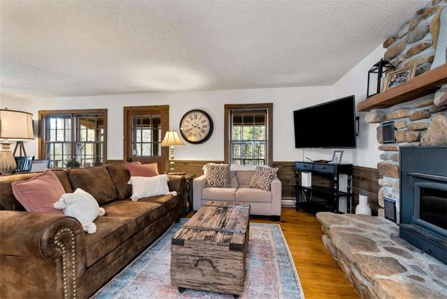 living room with a baseboard radiator, light hardwood / wood-style flooring, wood walls, a textured ceiling, and a fireplace