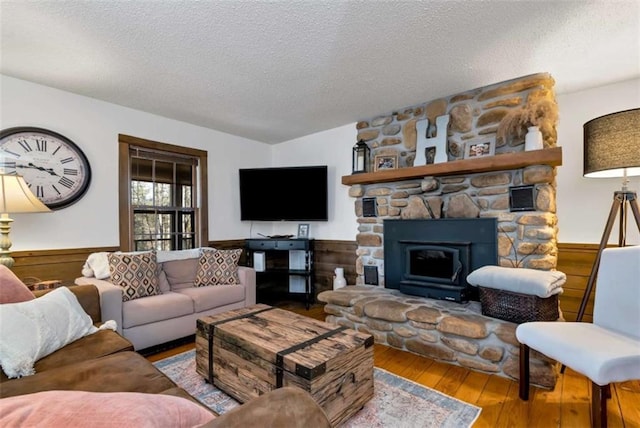 living room with a stone fireplace, wood walls, hardwood / wood-style floors, and a textured ceiling