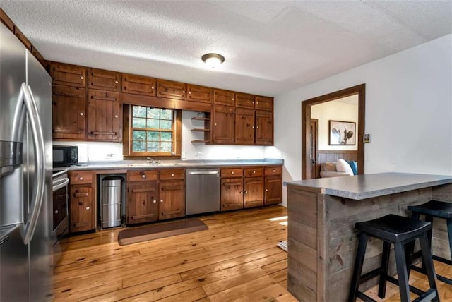 kitchen with appliances with stainless steel finishes, a textured ceiling, sink, light hardwood / wood-style flooring, and a breakfast bar area