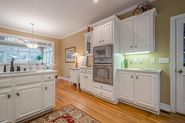 kitchen with appliances with stainless steel finishes, ornamental molding, light countertops, white cabinetry, and a sink