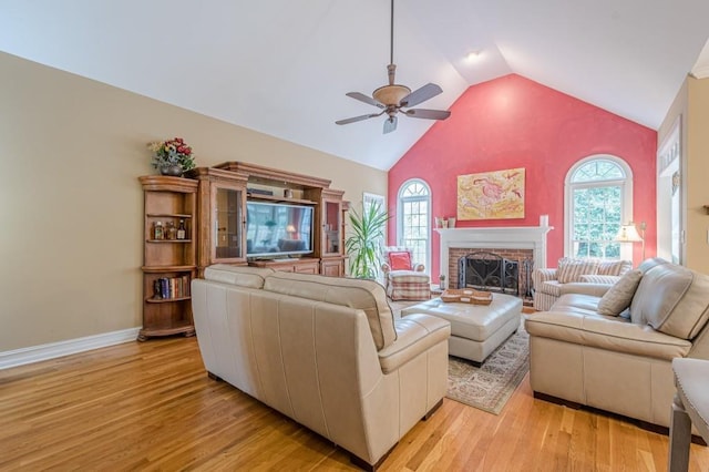 living area with ceiling fan, high vaulted ceiling, baseboards, light wood-style floors, and a brick fireplace