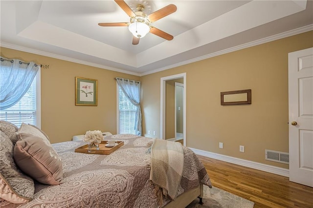 bedroom with ceiling fan, wood finished floors, visible vents, baseboards, and a raised ceiling