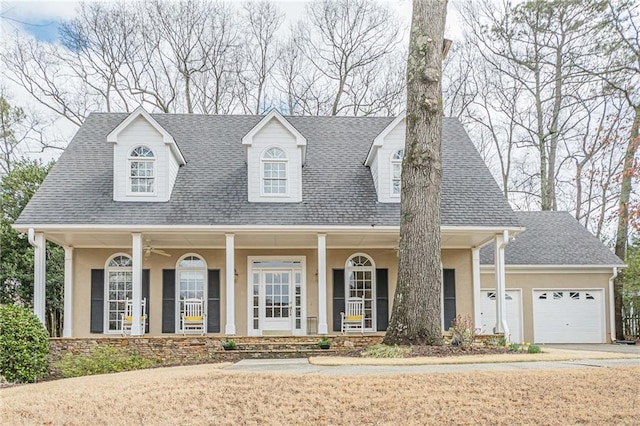 cape cod home featuring covered porch, a garage, a shingled roof, a ceiling fan, and stucco siding