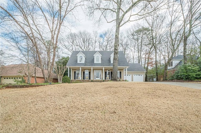 cape cod-style house featuring an attached garage, driveway, a porch, and a front yard