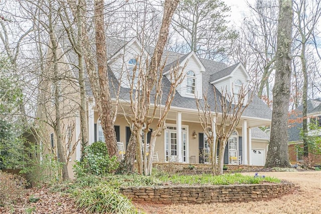 cape cod house with a shingled roof, a porch, and stucco siding