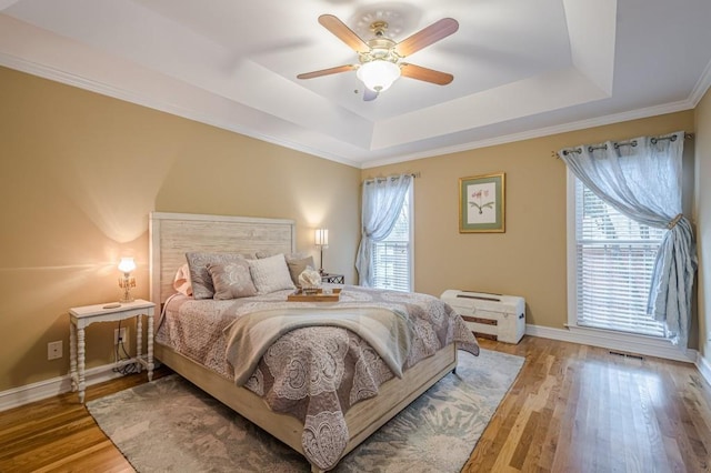 bedroom featuring baseboards, visible vents, ceiling fan, wood finished floors, and a tray ceiling