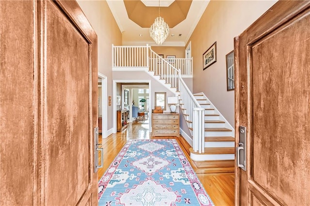 foyer featuring an inviting chandelier, a towering ceiling, ornamental molding, and light wood-type flooring