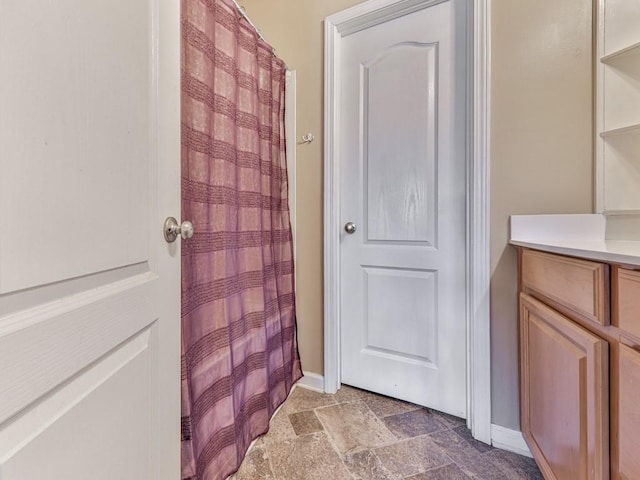 full bathroom with baseboards, stone tile flooring, and vanity