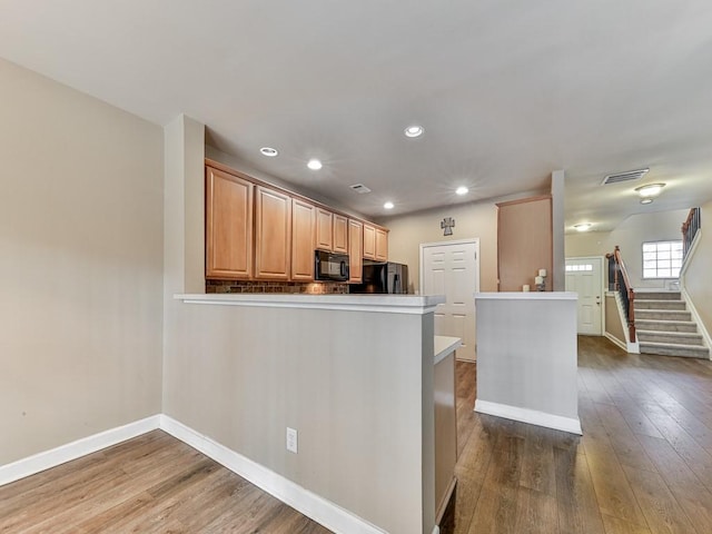 kitchen with black appliances, wood finished floors, light countertops, and visible vents