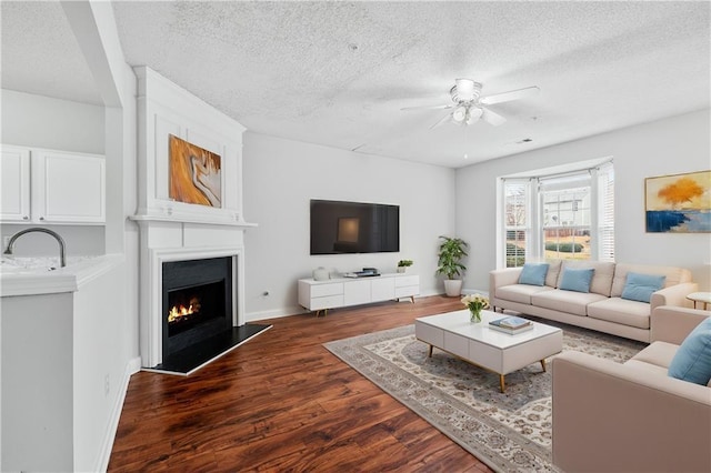 living room featuring ceiling fan, dark wood-type flooring, a large fireplace, and a textured ceiling