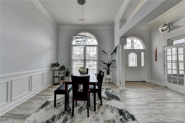 dining area with ornate columns, crown molding, and light wood-type flooring