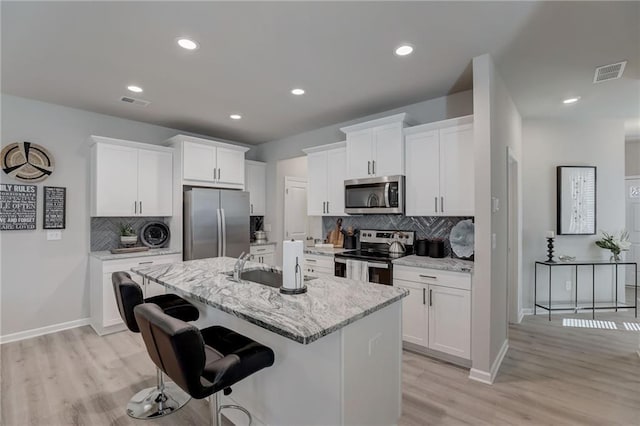 kitchen featuring light stone countertops, an island with sink, appliances with stainless steel finishes, and white cabinets