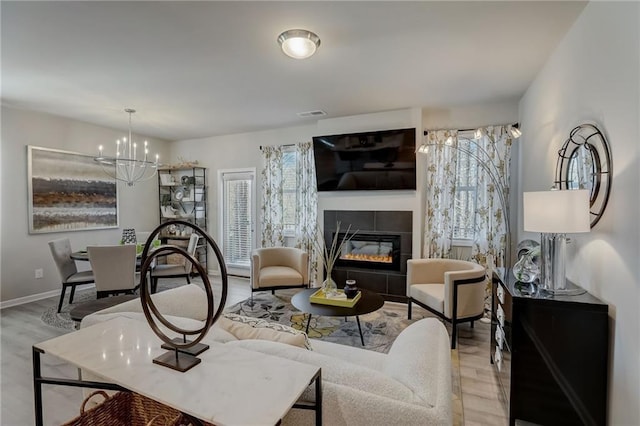 living room with an inviting chandelier, a tiled fireplace, and light hardwood / wood-style flooring