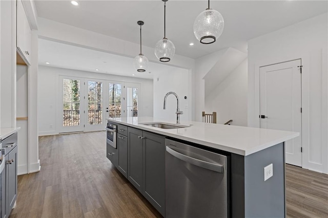 kitchen featuring a center island with sink, appliances with stainless steel finishes, sink, gray cabinetry, and hanging light fixtures