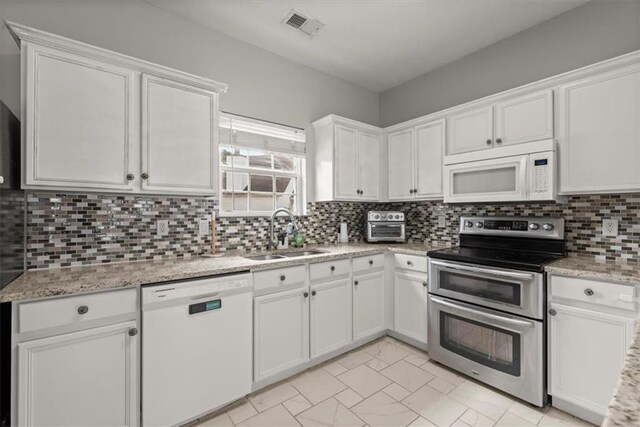 kitchen featuring tasteful backsplash, light stone counters, white appliances, sink, and white cabinets